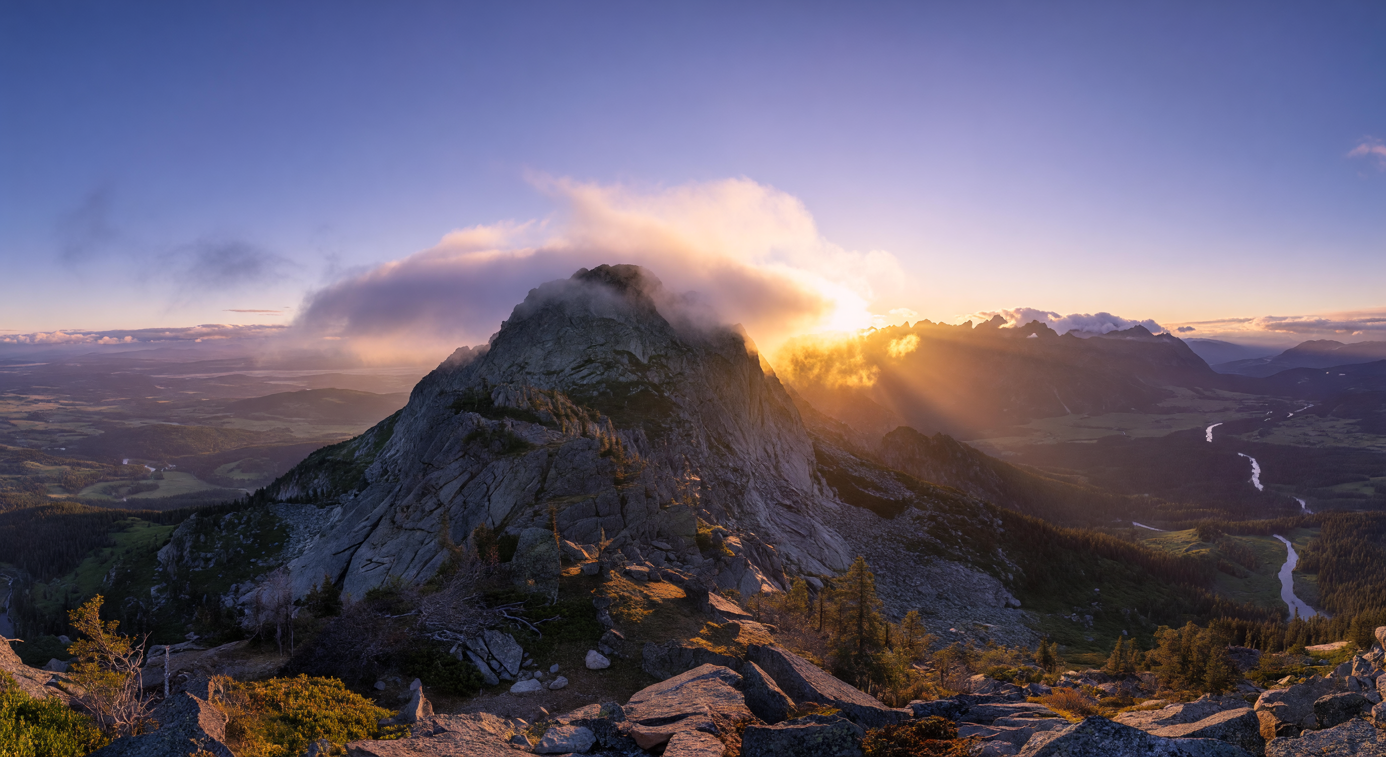 A mountaintop at dawn wreathed in low cloud, the first gold of sunrise breaking over a distant ridge, vast and wild landscape below
