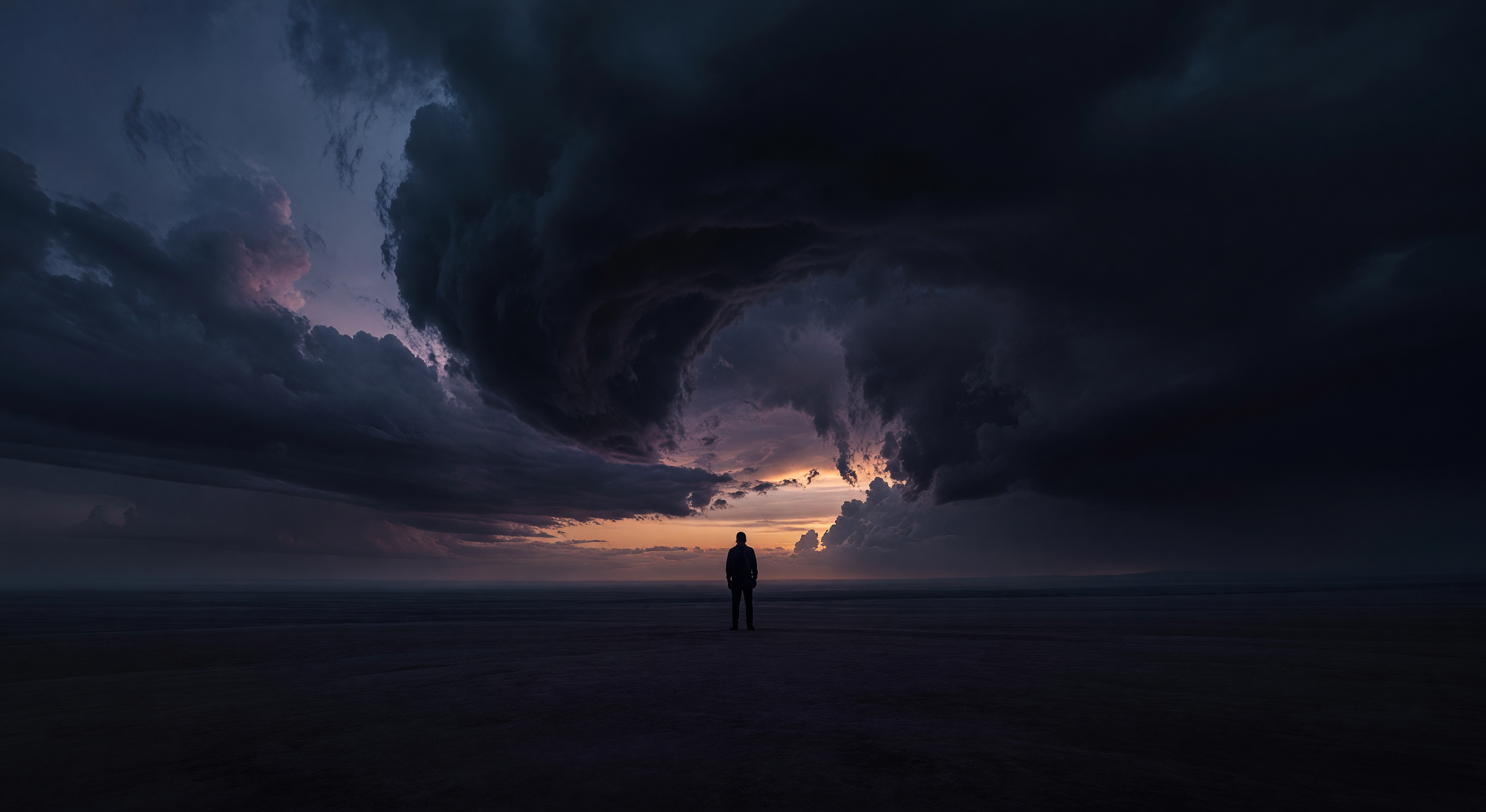 A lone figure silhouetted against a vast twilight sky with dramatic clouds, looking out over an empty landscape